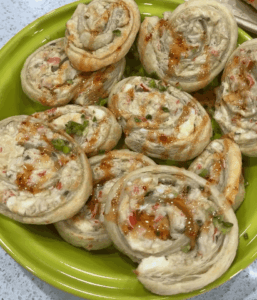 Crab rangoon puff pastry rolls baked golden and topped with sweet Thai chili sauce and chopped green onions on a green serving plate.